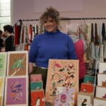 Smiling stallholder in front of their stall of artwork