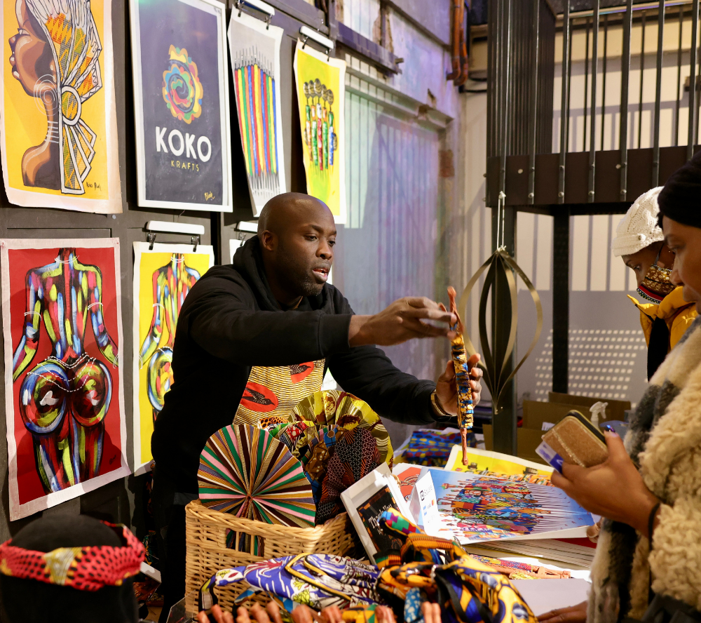 Stallholder stood looking at an art stall. Black Culture Market