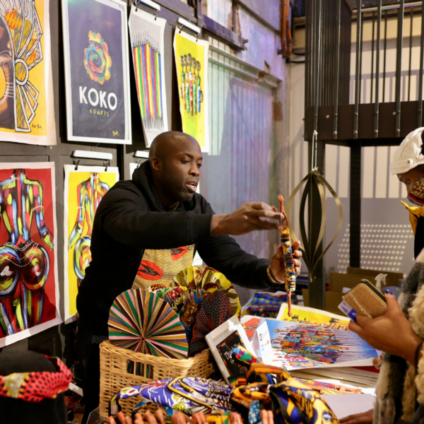 Stallholder stood looking at an art stall. Black Culture Market