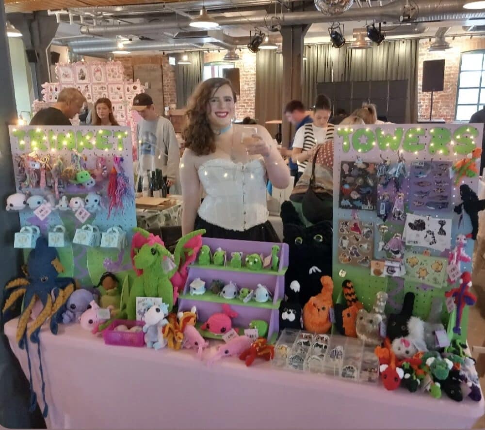 Smilling stallholder at stall showing crocheted animals