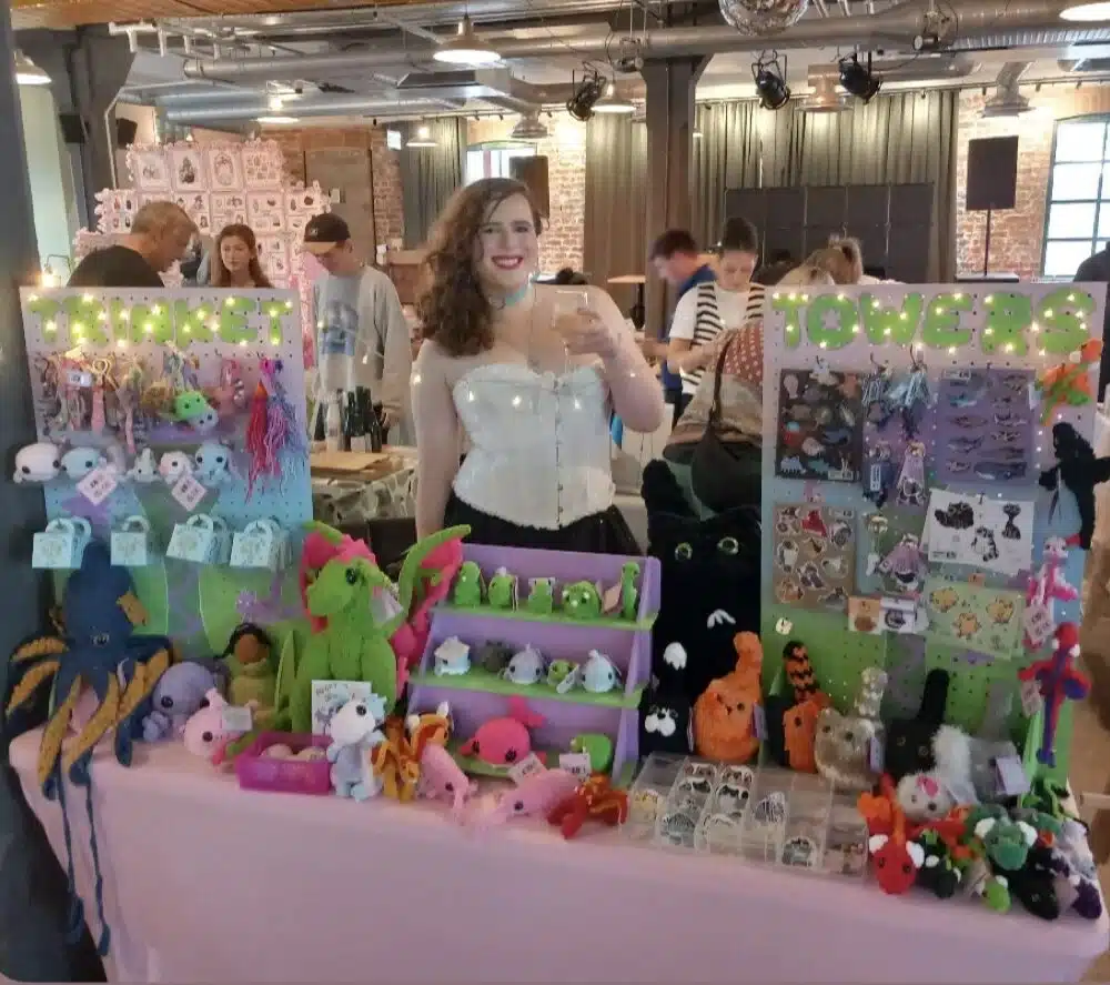 Smilling stallholder at stall showing crocheted animals
