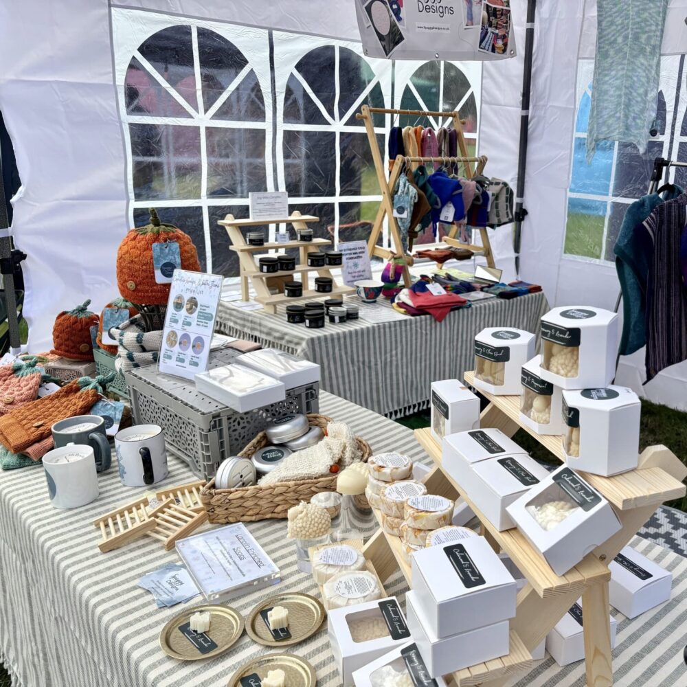 Outdoor market setup: white gazebo with soap and candle displays, and knitwear rails.