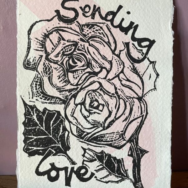 Mandy Benton Printmaker, 'Sending Love' Linocut Print. A small linocut print on a beautiful handmade paper depicting roses and the message 'Sending Love'. Printed in black ink over a sweep of pink watercolour paint.
