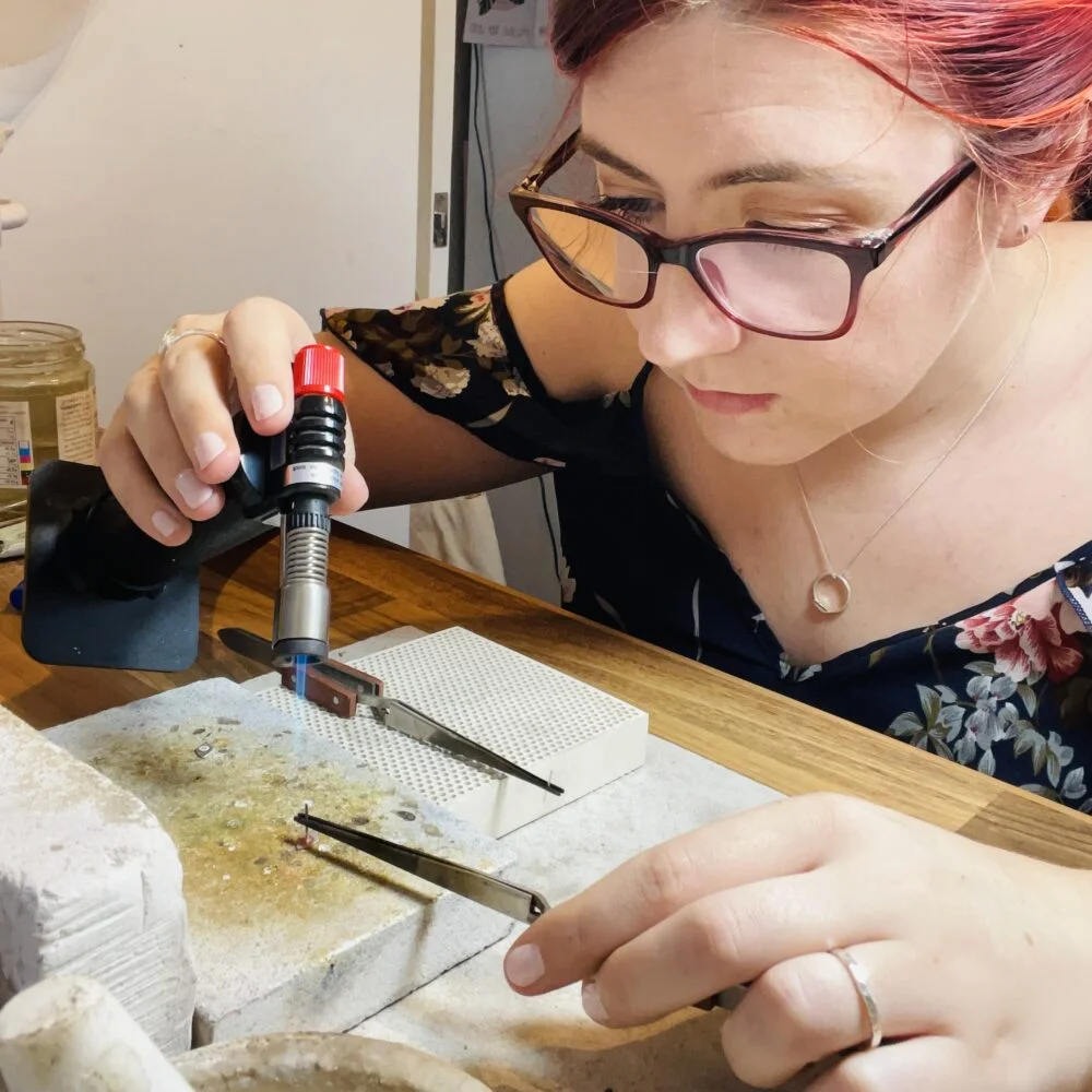Jen Lithgo woldering a pair of stud earrings in her home studio