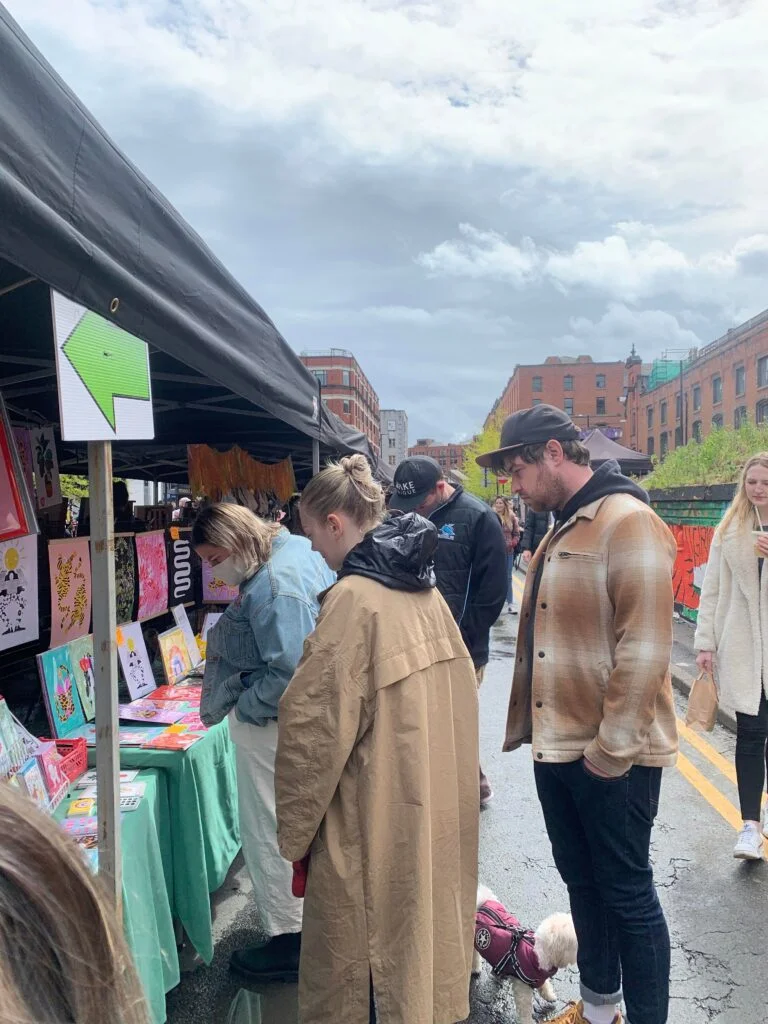 Customers gathered around a stall, looking at colourful art prints at Northern Quarter Makers Market in Manchester