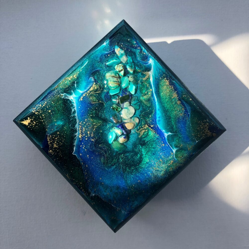 These fabulous trinket boxes are a work of art with each piece having it own unique epoxy resin design. No one piece is ever the same so you can be sure to have a one of a kind piece of artwork which allows you to store small items. This small square hinged wooden box with a magnetic closure, has been hand painted with dark metallic turquoise acrylic paint and wax varnished. The epoxy resin decoration contains natural gemstone shards consisting of Amazonite, Lapis Lazuli and Turquoise. This piece also consists of 3 pigments and gold powder, thus creating a decorative impression of a stoney ocean. The Inside has been lined with waterproof velvet giving a luxurious feel to the inside of this stunning little trinket box. Making it into a wonderful addition to any setting, and an ideal gift for that someone special. Trinket Boxes can also be made to order