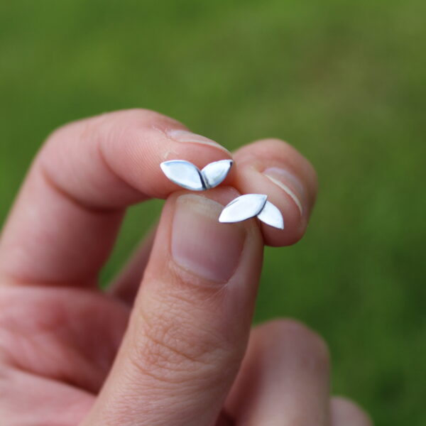 Sterling silver duo Leaf studs in pinched fingers with grass in the background