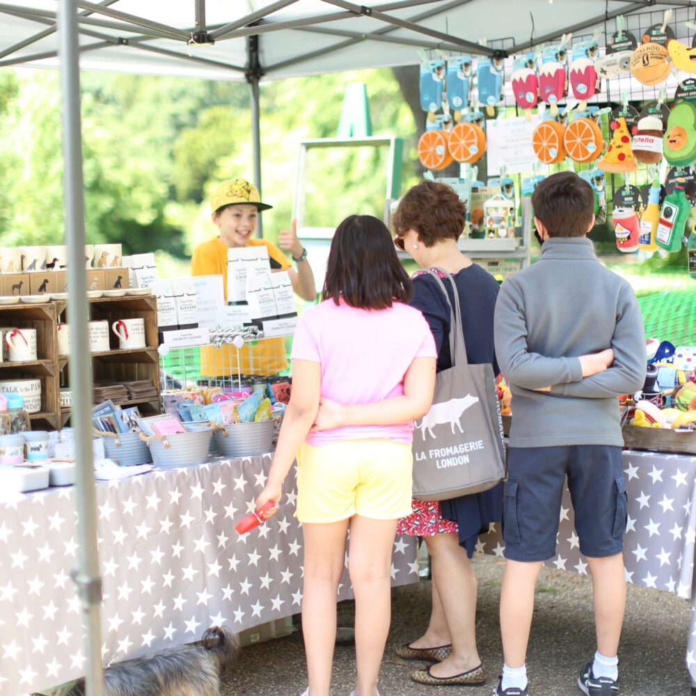 Young stallholder serving 3 customers at Duck Pond Market, Chiswick House Artisan Market