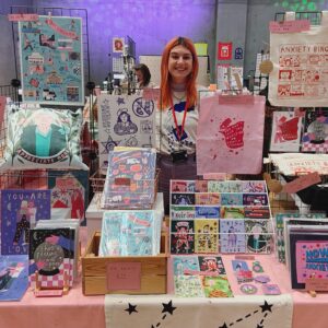 Colourful market stall in Nottingham showing Ella kasperowicz and her prints, illustrations, tote bags, postcards and tees.