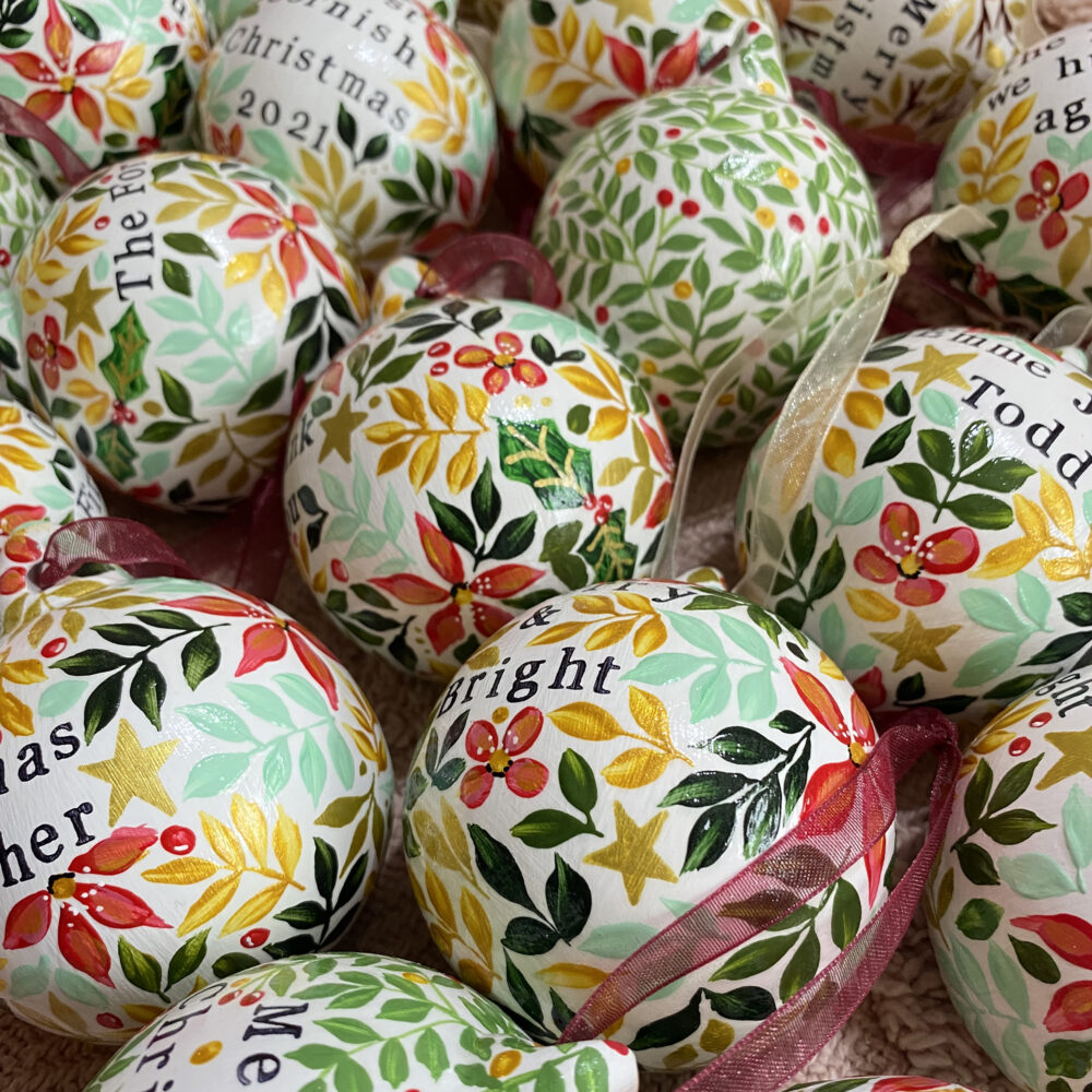 Personalised hand painted ceramic christmas baubles in red and green floral designs by Ellie Cartlidge Design