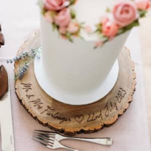 Laser-engraved wooden wedding cake stand featuring a personalised couple's name and date, with a heart design.