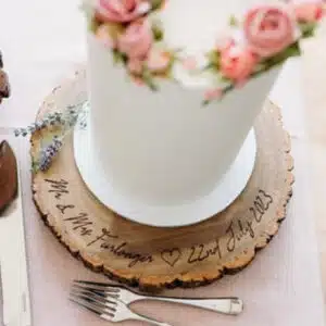 Laser-engraved wooden wedding cake stand featuring a personalised couple's name and date, with a heart design.