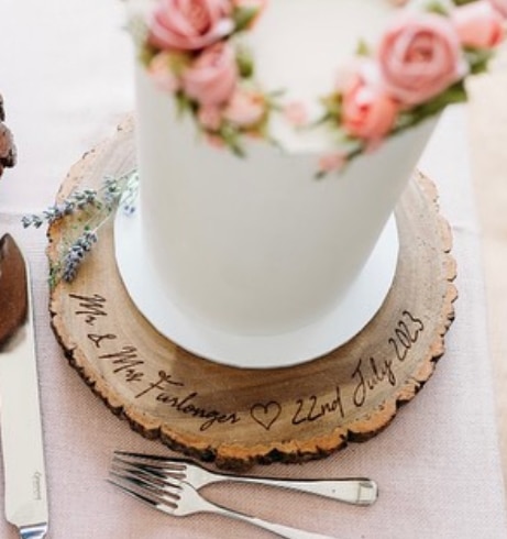 Laser-engraved wooden wedding cake stand featuring a personalised couple's name and date, with a heart design.