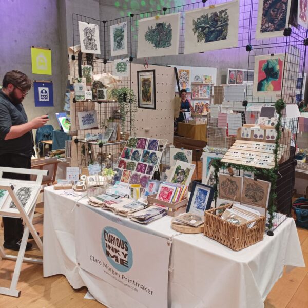 Curiousinkyme - Print fair stall set up with a table full of lino cut artworks. nature and floral.