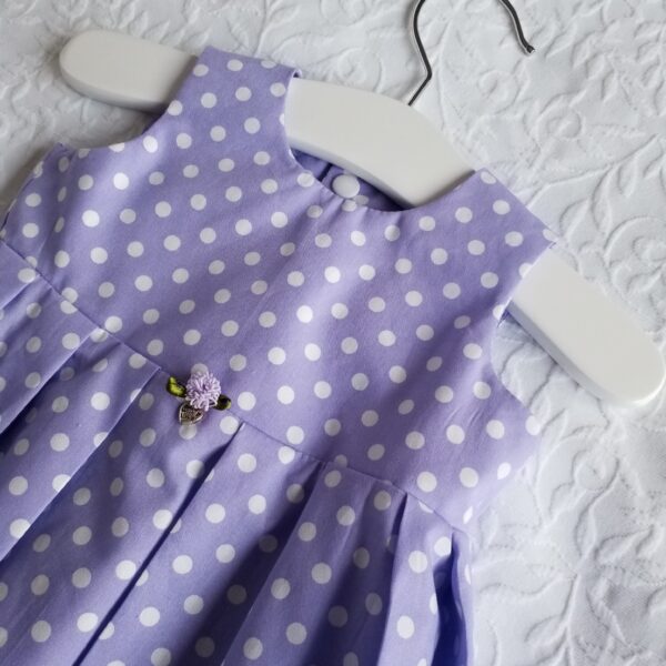 Lilac polka dot hand made dress in premium cotton. Has flower decoration at front. The bodice is lined and the skirt is full. The back has 4 popper fasteners for easy dressing. Available in sizes 3 months to 12 months.