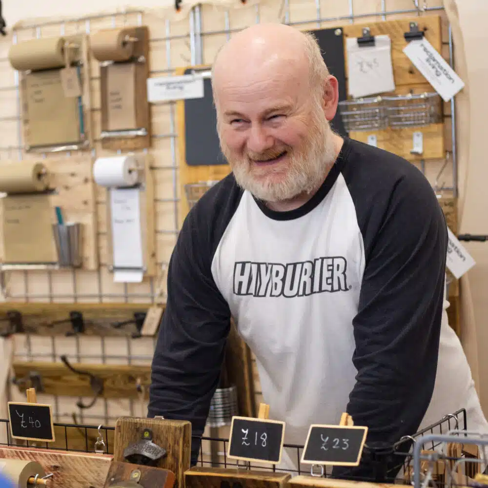 Independent maker smiling behind a stall of handmade wooden gifts and homewares at a Paper Daisy Events makers fair in Shoreham.