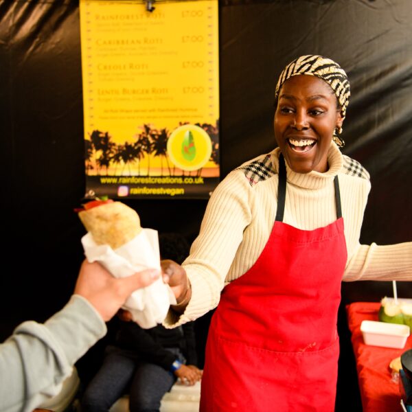 A smiling lady in a red apron hands a sandwich to a customer