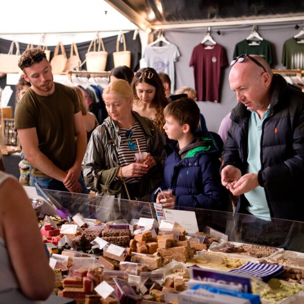 People browse a fudge and sweet stall at an indoor market.
