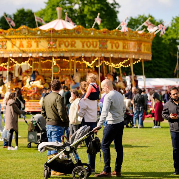 A vintage carousel on grass with families milling around.