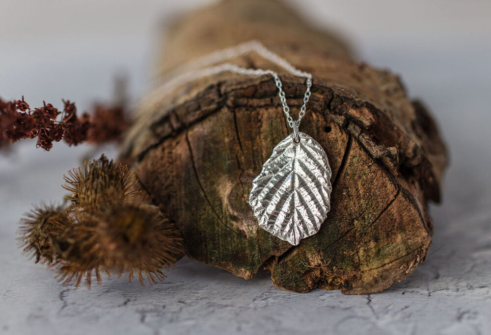 Silver blackberry leaf necklace resting on brown branch