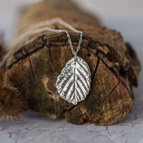 Silver blackberry leaf necklace resting on brown branch