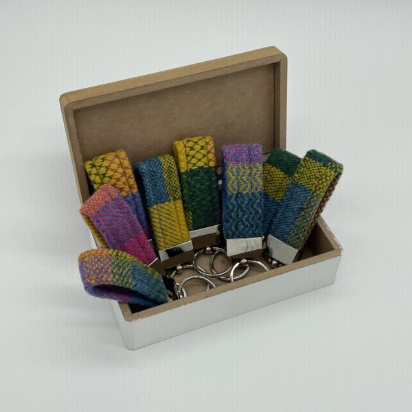 An open wooden box displaying a selection of brightly coloured key fobs By Hook & Heddle
