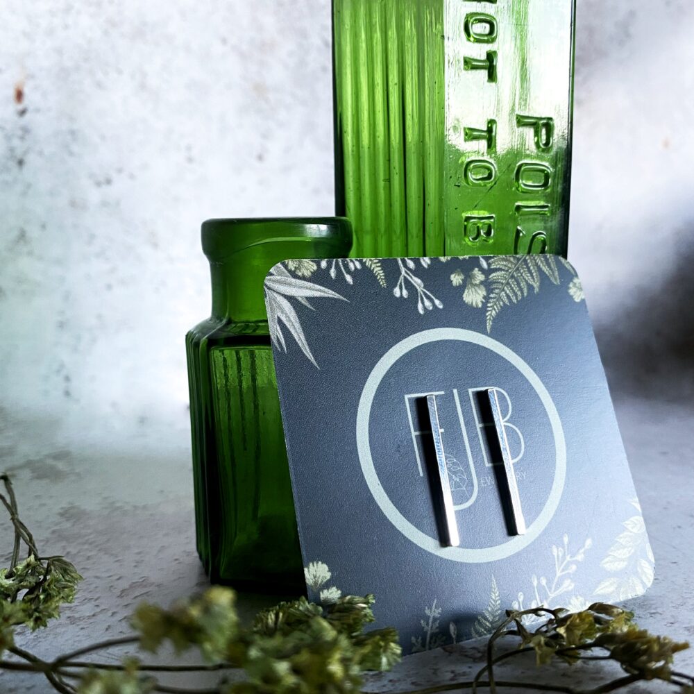 A pair of minimal style long vertical bar sterling silver stud earrings. Display on a dark green square card showing the Fran Barnett Jewellery logo