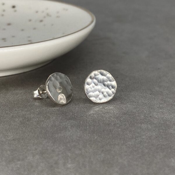 Round silver stud earrings with a dimpled, hammered finish. One is side on so you can see the post and butterfly back.