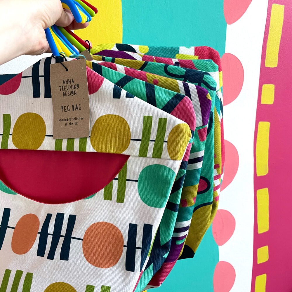 A Hand holding 6 colourful peg bags in front of a colourful wall mural.