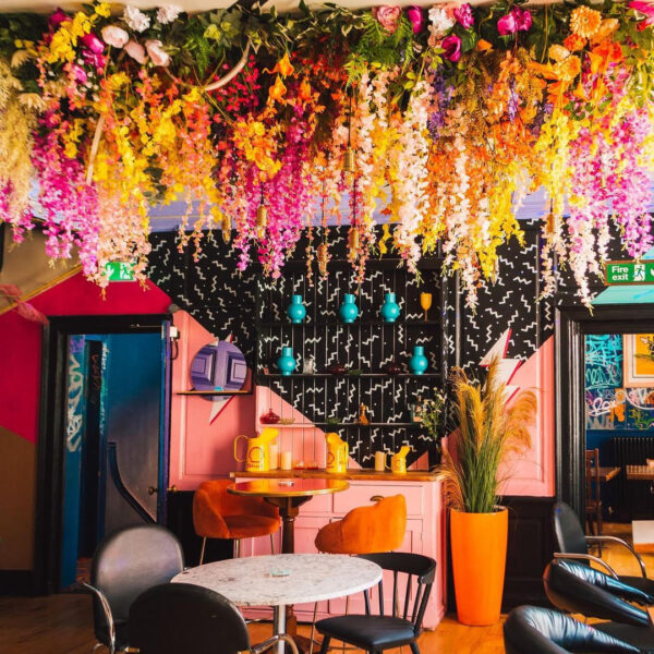 image of the venue the magic garden with bright walls painted in geometric shapes. floral arrangement draping from the celiing in yellows and pinks create a dramatic effect above a marble round table