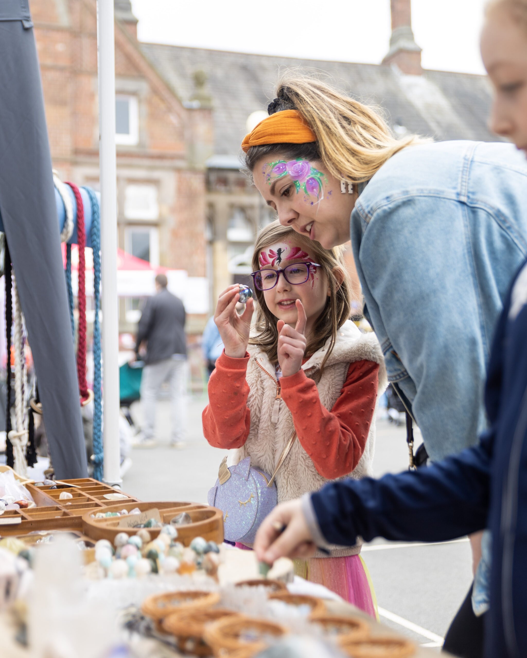 image shows people browsing a stall with colourful face paint on