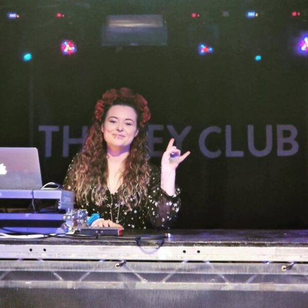 image shows Leeds Indie Market organiser Courtney stood on the stage at The Key Club, their logo is displayed on a flag in the background.