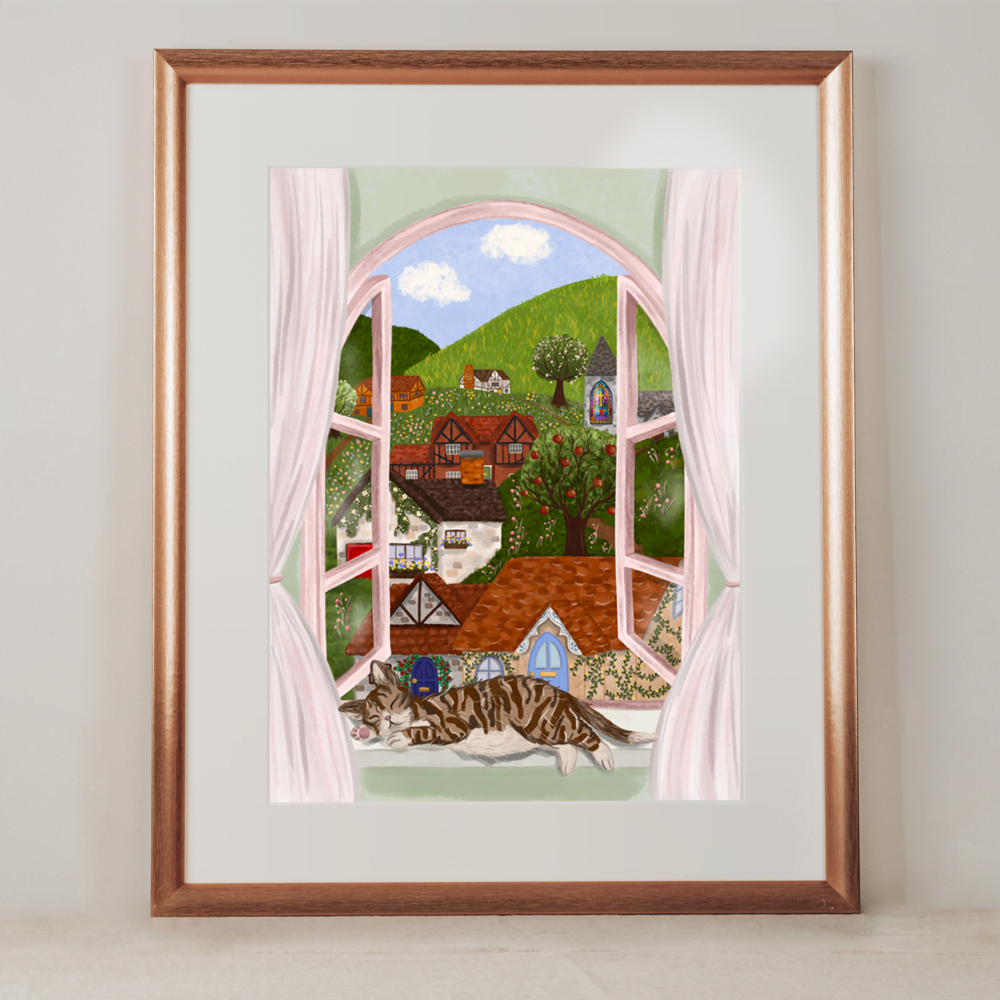 A framed photo of a digital illustration. The illustration features a window which looks out to a quaint fairytale village. There is a cat asleep on the windowsill and soft pink curtains blow in the breeze.