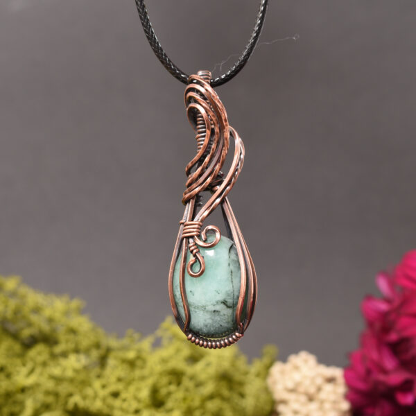 Antiqued copper wire wrapped pendant featuring an emerald cabochon suspended on a black cord