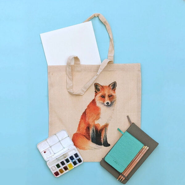 A tote bag with my Fox printed on with some art supplies surrounding it.