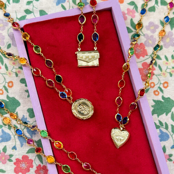 Four gold lockets, with colourful bubble chain sit in a shallow lilac box with a red velvet background. The box is sitting on a colourful floral fabric background. Shop Gwynfor