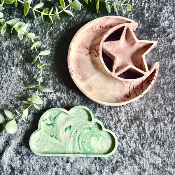 A green cloud shaped tray and a pink moon and star shaped tray on a grey velvet background