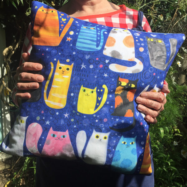 photo of someone holding a cushion printed with colourful illustrations of cats