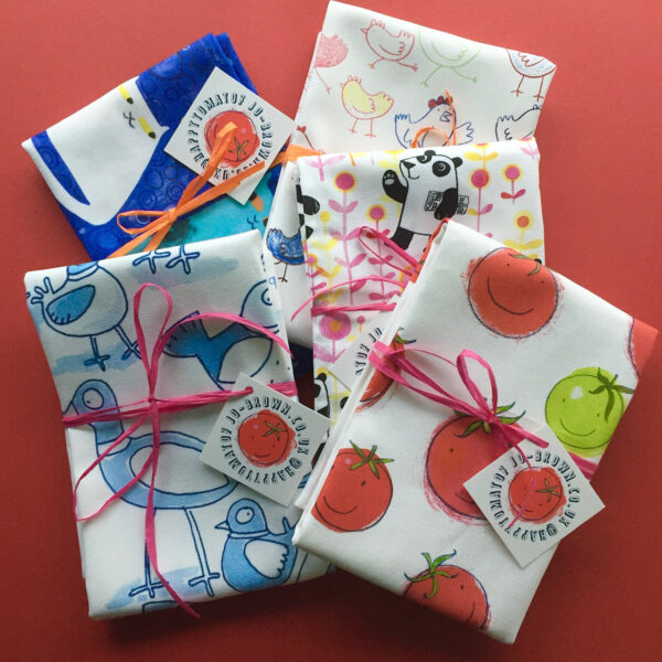 five printed tea towels with different designs, by Jo Brown, folded and tied with paper tape and tags.