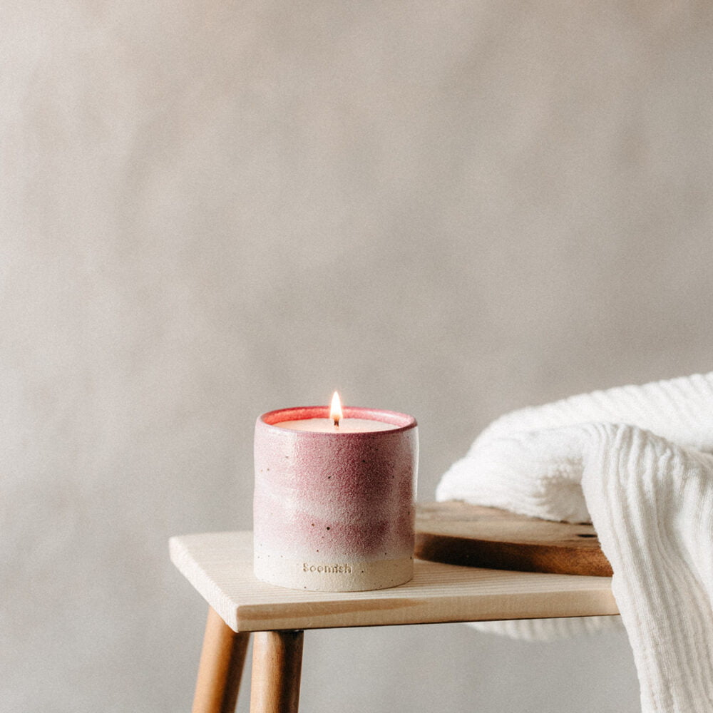 A ceramic pot with a lit soomish candle. Pot glaze is pick and creams - Soomish