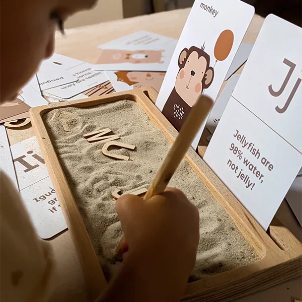 Toddler drawing letters in sand in a Montessori play set up with Animal Alphabet Flashcards from kids brand Paper & Bean