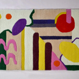 Image shows a cream rug with multicoloured abstract shapes on it. These shapes are red, burgundy, sunflower yellow, hot pink, dark green and orange. the background of the rug has 2 beige block colour sections. The rug is photographed against a very pale pink background.