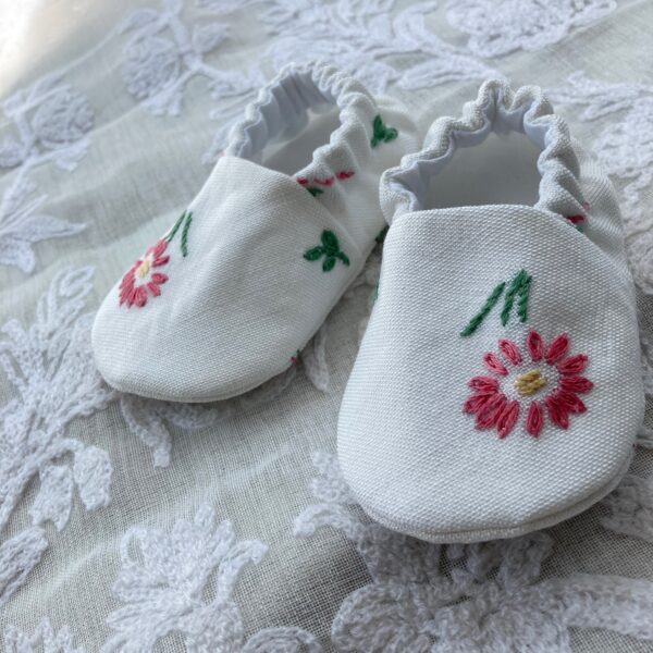 A pair of white baby shoes with floral embroidery, handmade from a vintage tray cloth by Happy Hedgehog Designs