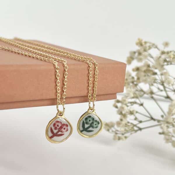 A small red floral necklace and a small green floral necklace hanging off a jewellery box