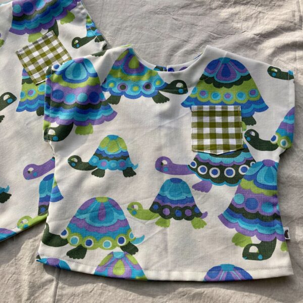 A white top for a baby or toddler made from a vintage cot sheet featuring purple, blue and green tortoises, Happy Hedgehog Designs