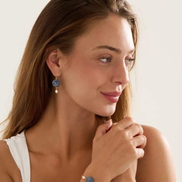 Female model wearing blue dangle earrings with a pearl, and a dainty blue bracelet