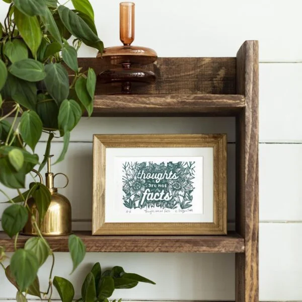 Small artwork on shelf featuring thoughts are not facts quote in green botanicals