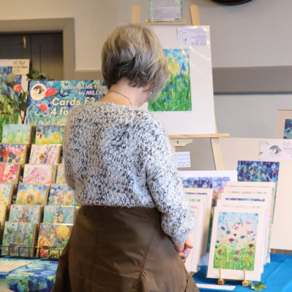 Customer browsing an art stall with floral alcohol ink paintings at Tissington Craft Fair in Derbyshire, Tissington Craft Fairs
