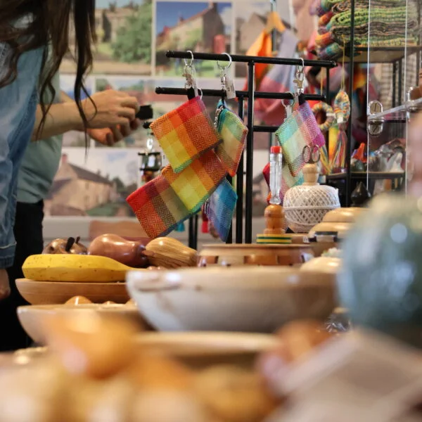 Customers are looking at a piece of jewellery in a box at Tissington Craft Fair in Derbyshire. You can also see wood turned items and woven textiles in the foreground. Tissington Craft Fairs