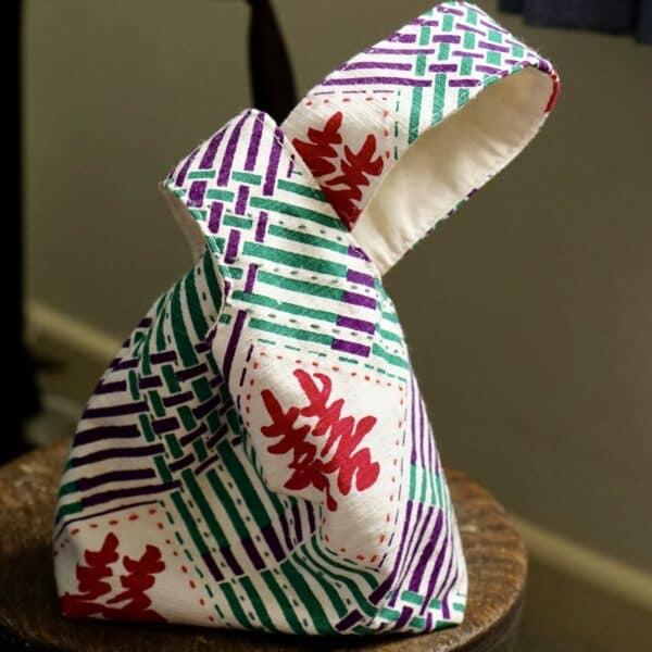 A fabric knot bag placed on a small bench, the fabric has double happiness motif in red colour.